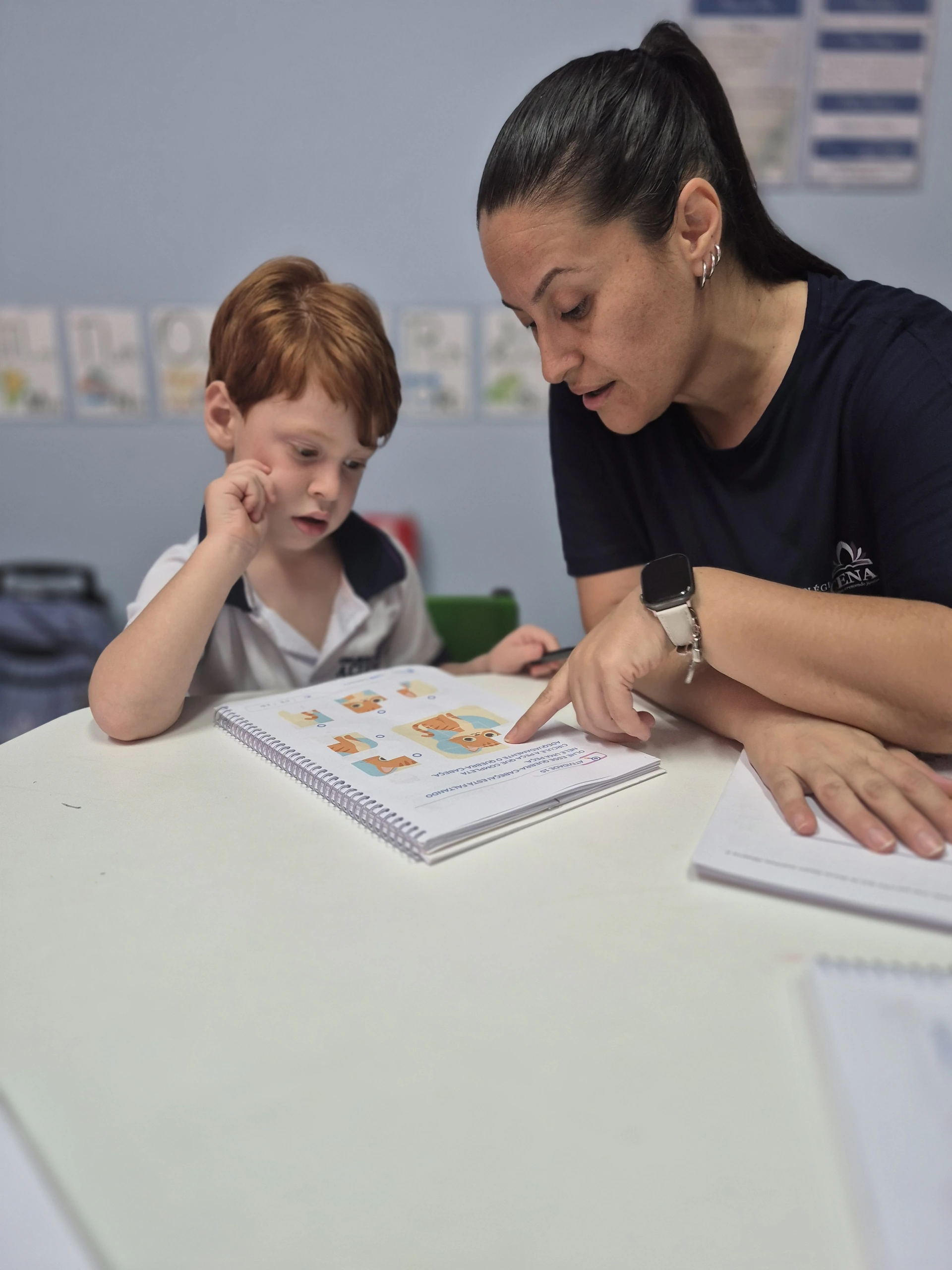 Professora acompanhando um aluno individualmente durante atividade no caderno