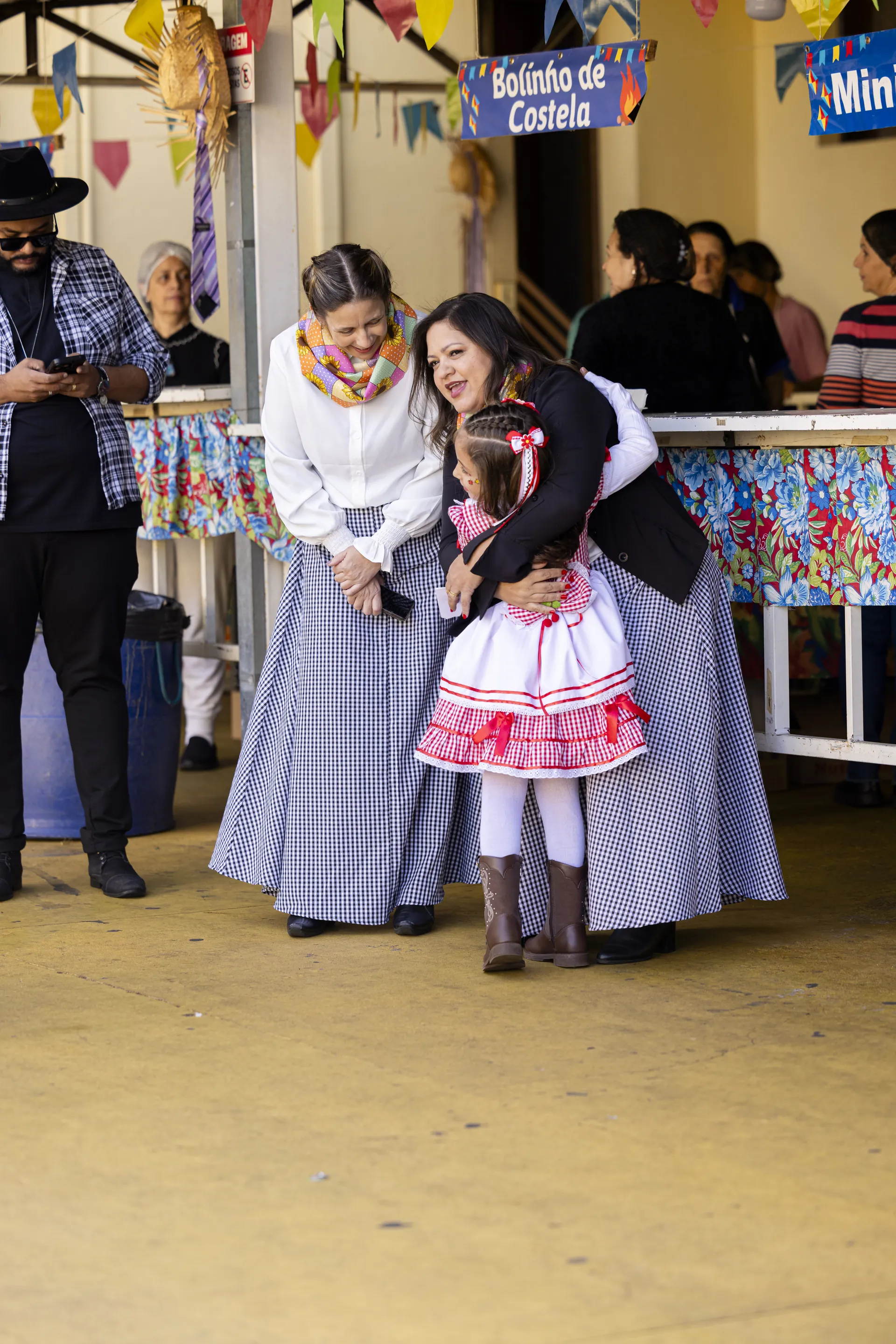 Professoras acolhendo uma aluna durante festa da comunidade escolar