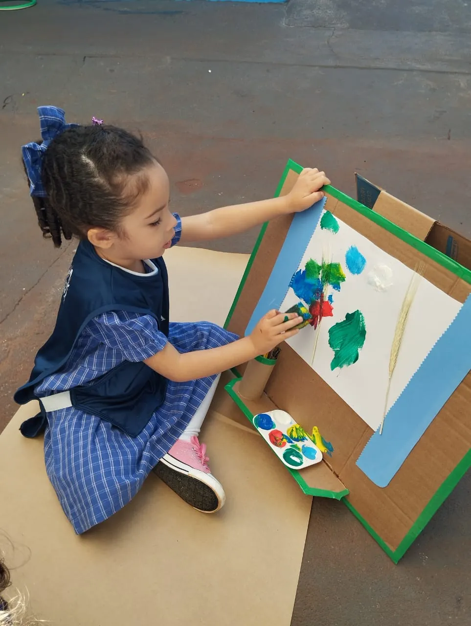 Aluna pintando com autonomia em cavalete no pátio
