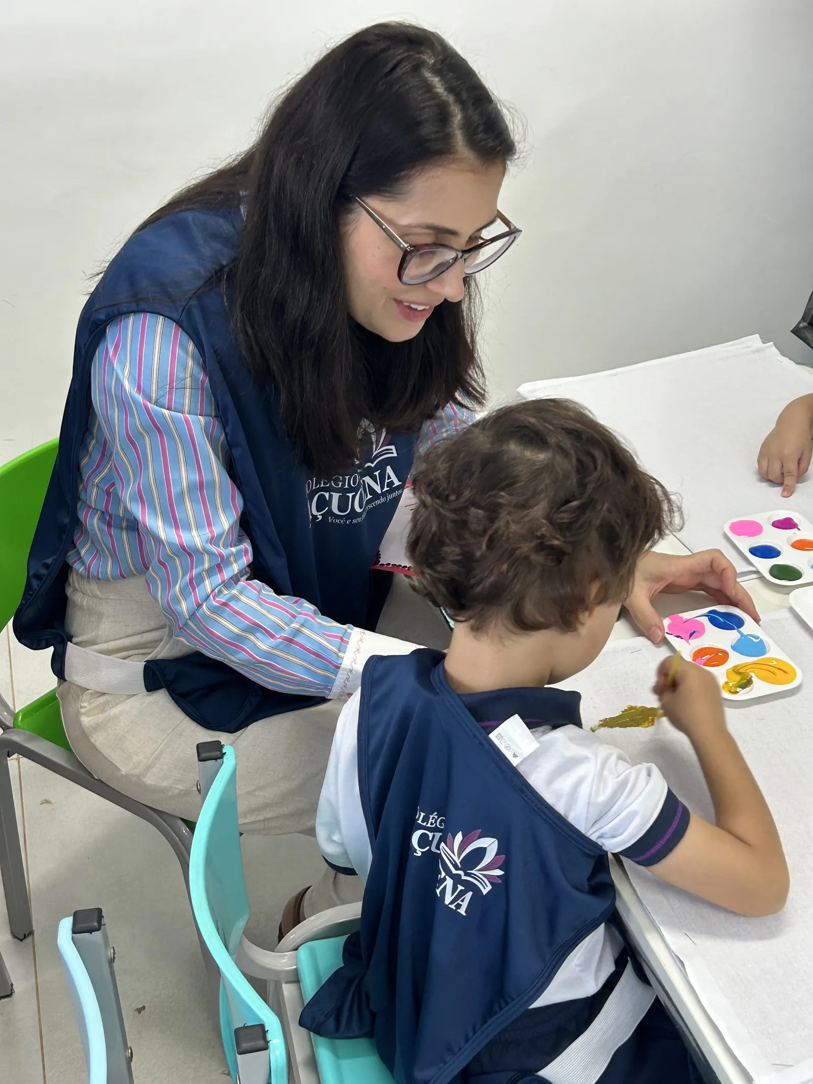 Professora orientando de perto um aluno durante atividade de pintura