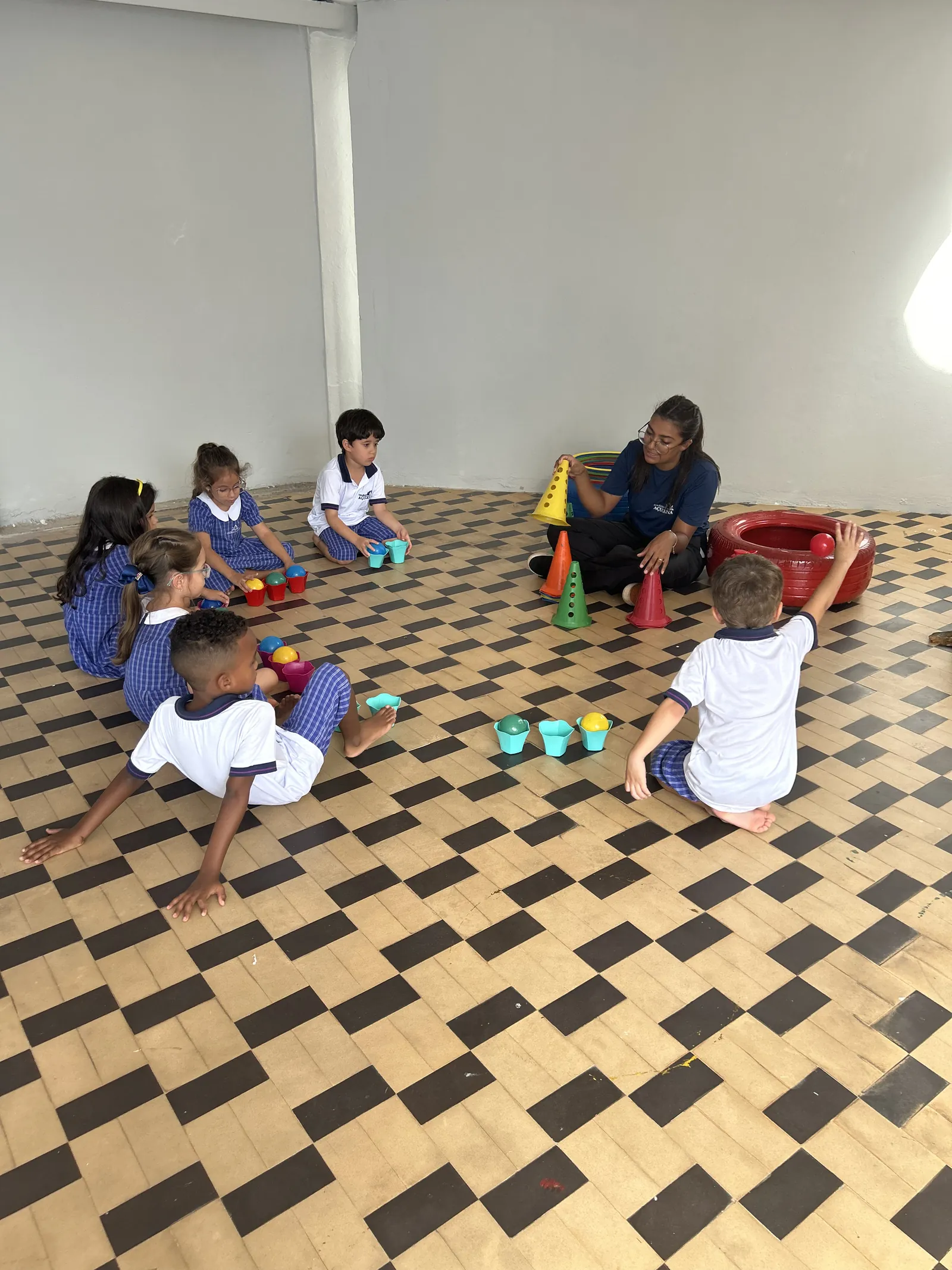 Aula prática em grupo: crianças e professora em atividade com cones e bolinhas