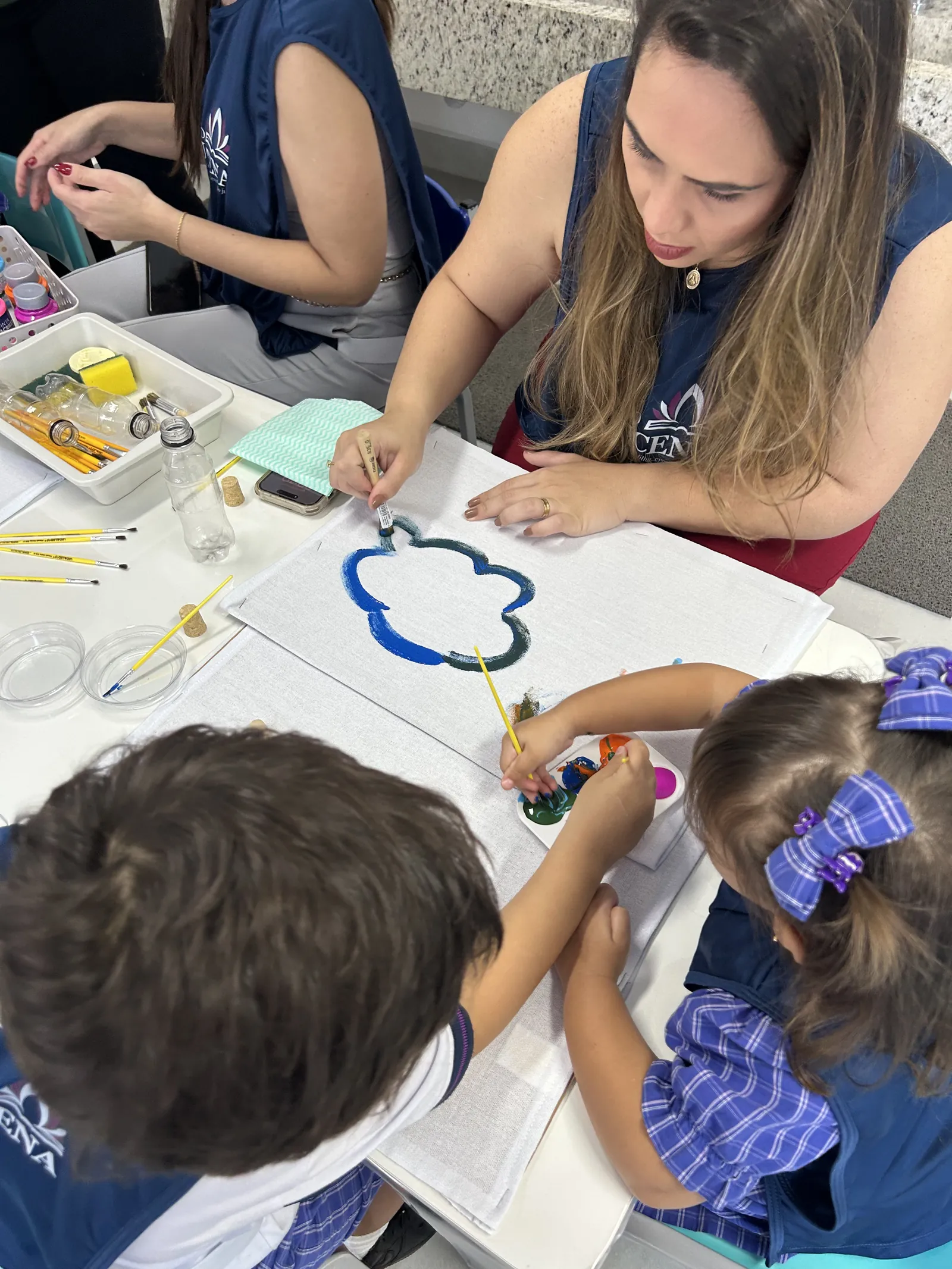 Professora e alunos pintando juntos em atividade de artes