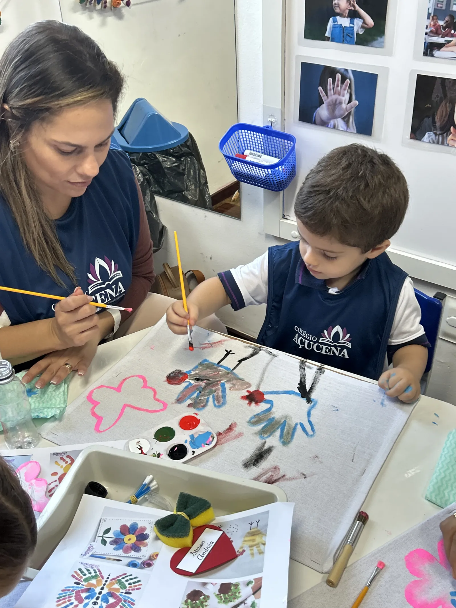 Professora acompanhando aluno em atividade de pintura na sala de aula