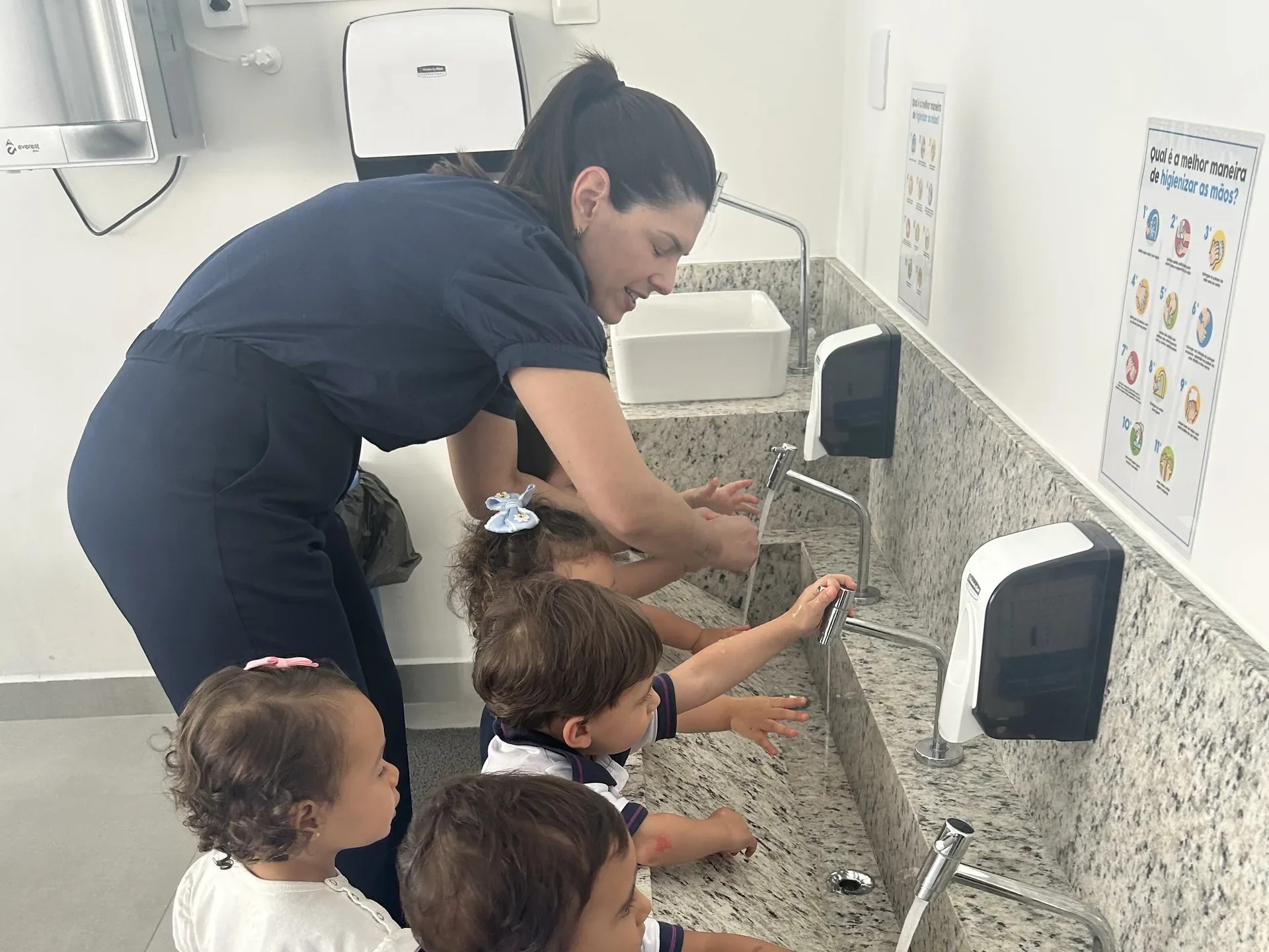 Professora ajudando crianças pequenas a lavar as mãos em pias adaptadas à altura delas